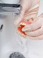 Eine Vollprothese wird unterm Wasserhahn gesaeubert